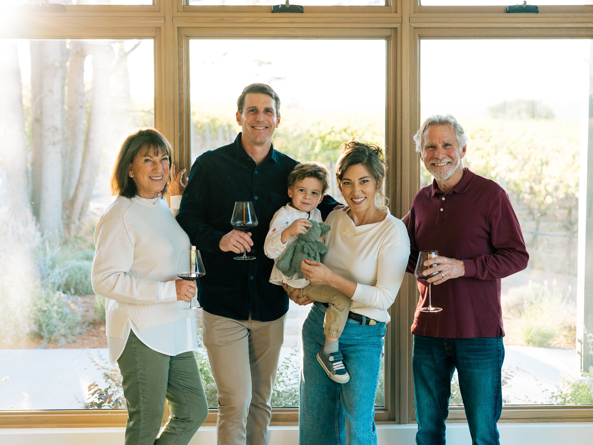 The Kanzler Family of four with a baby standing in front of large windows with a scenic view holding glasses of Pinot Noir.