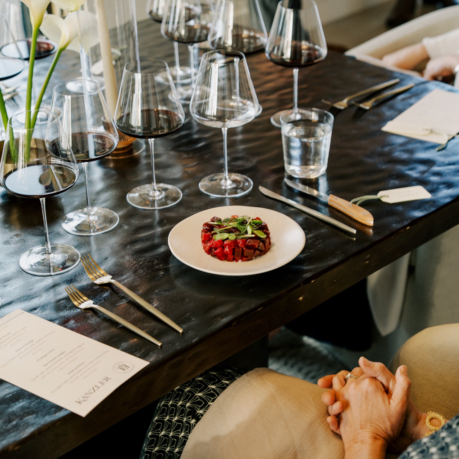 Kanzler dining table set for a meal with wine glasses, plates, and cutlery.